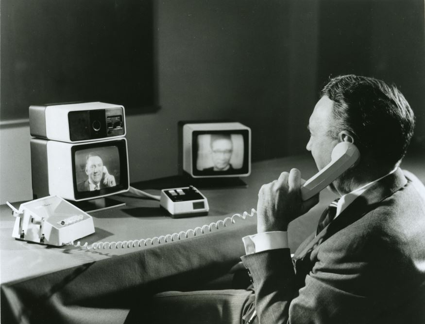 A man talks on the photo while being able to see himself and his meeting partner on small televisions