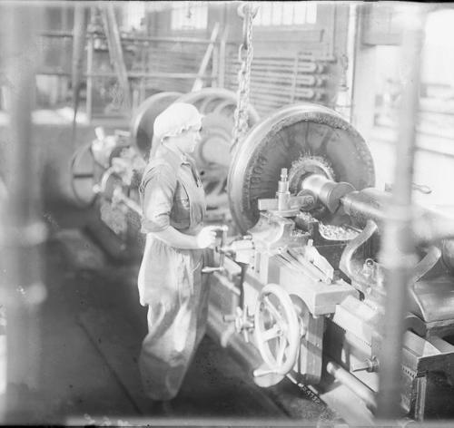 Black and white image of a woman in a machine shop, working at a large lathe machine.