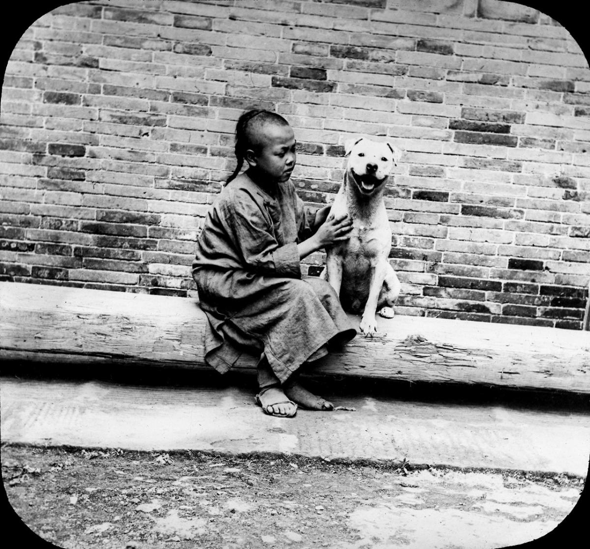 A lantern slide from the Ferracute Machine Company, depicting an unidentified child sitting with Snooks the dog in China, 1898.