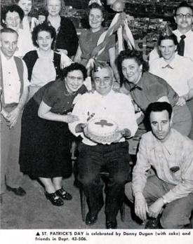 A black and white photograph depicts a group of people celebrating St. Patrick's Day, with a man holding a cake.