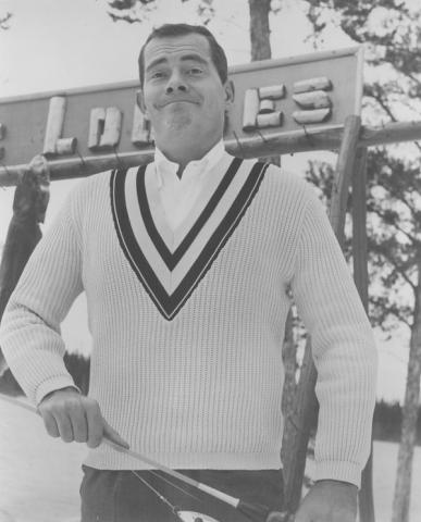 The image features a man wearing a sweater and standing outdoors. The photo is in black and white.