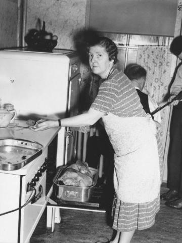 Black and white photograph of an older woman removing a turkey from an oven