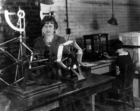 The image shows a woman working in a textile factory, depicted in black and white.