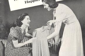 Pamphlet cover. Black and white photo of a woman displaying a dress on a hanger to another woman seated on a couch.