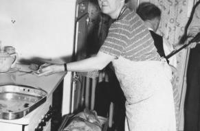 Black and white photograph of an older woman removing a turkey from an oven